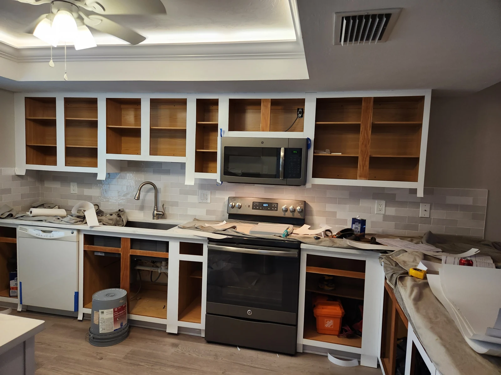 The same kitchen during refacing, doors removed, retained boxes exposed and tools on the counter