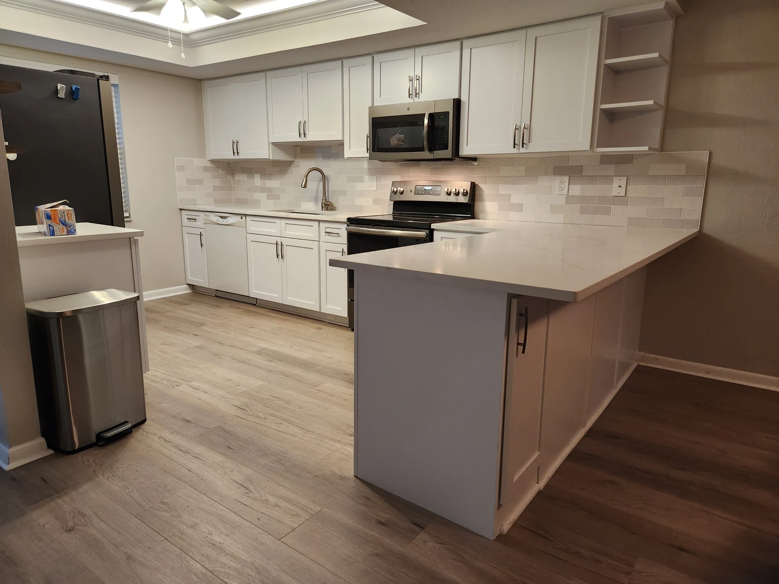 The same kitchen with white cabinet fronts and metal pulls fitted along the main run